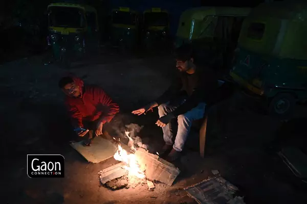 As seen in this photograph, two autorickshaw drivers are seen basking in heat from a small fire that they have arranged at their auto-stand.